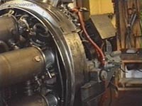 A view looking toward the drive end of the engine, showing (partially) three of the eight inter-linked combustion chambers. Fuel and air mix flows right-to-left in this picture, igniting by means of igniters in a few of the cylinders, and the flame allowed to propagate through to non-igniter cylinders by means of two flame ducts on each cylinder. You can see these in the form of grey pipes connecting each combustion cylinder. <br><br>Fuel is injected at the head of each cylinder at high pressure and mixed with high pressure air from the compressor by means of a fan-shaped device at the intake. Combustion occurs and the fuel/air mix expands down the cylinder (toward the left here), and is output onto the high pressure turbine at its end. It is the output from this turbine which drives the compressor, and provides useable power to the drive shaft, hydraulic systems and electrical generators. The engine exhausts via an exhaust pipe out of the back of the craft.